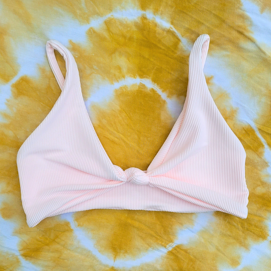 Pink ribbed bikini top on a yellow and white tie-dye background.